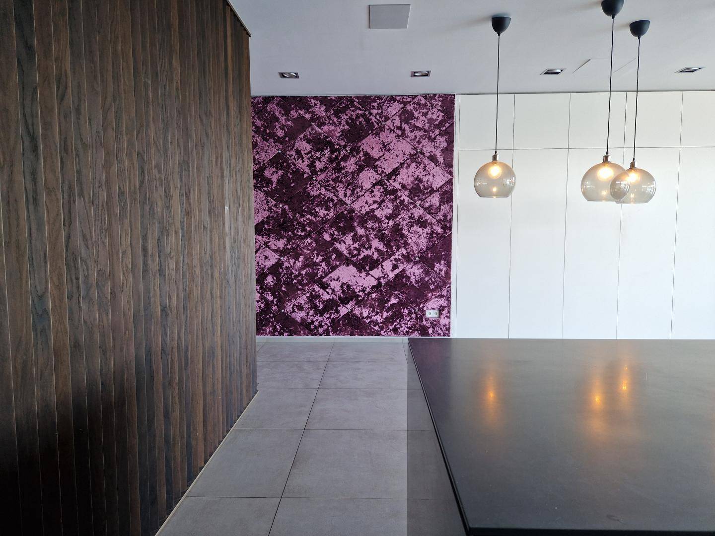 Küchenbereich mit dunkler Kücheninsel, Holzwand und auffälliger lila Akzentwand.