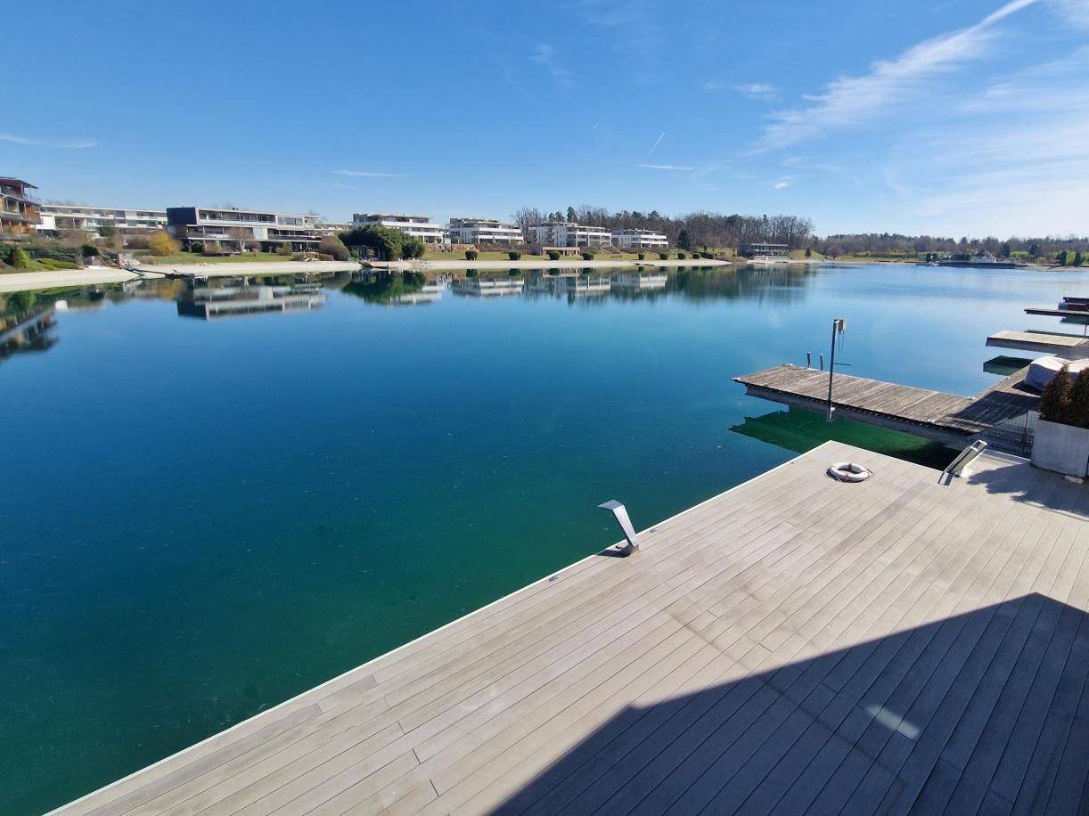 Weitläufige Holzterrasse am Seeufer mit Blick auf moderne Gebäude und Stege.