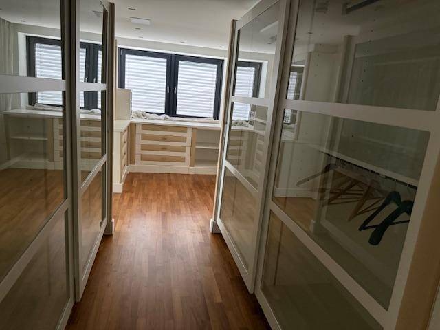 Geräumiger begehbarer Kleiderschrank mit Holz- und Glaselementen sowie Fenster.