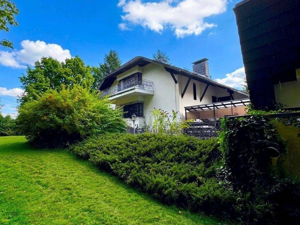 Großzügiger Garten mit Rasenfläche, überdachter Terrasse und Balkon am Haus.