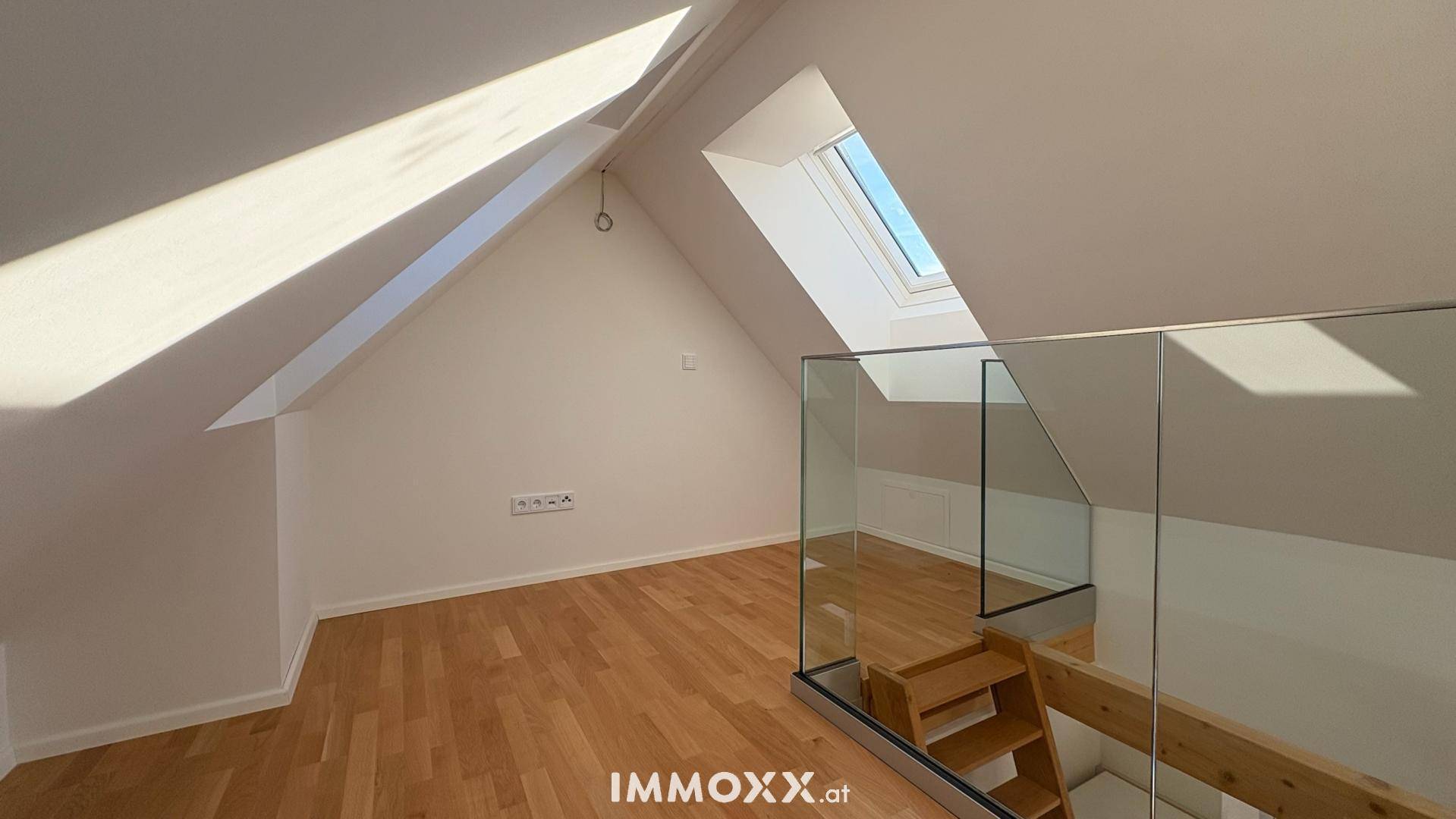 Heller Dachbodenraum mit Holzboden, Dachfenster und moderner Glasbrüstung zur Treppe.