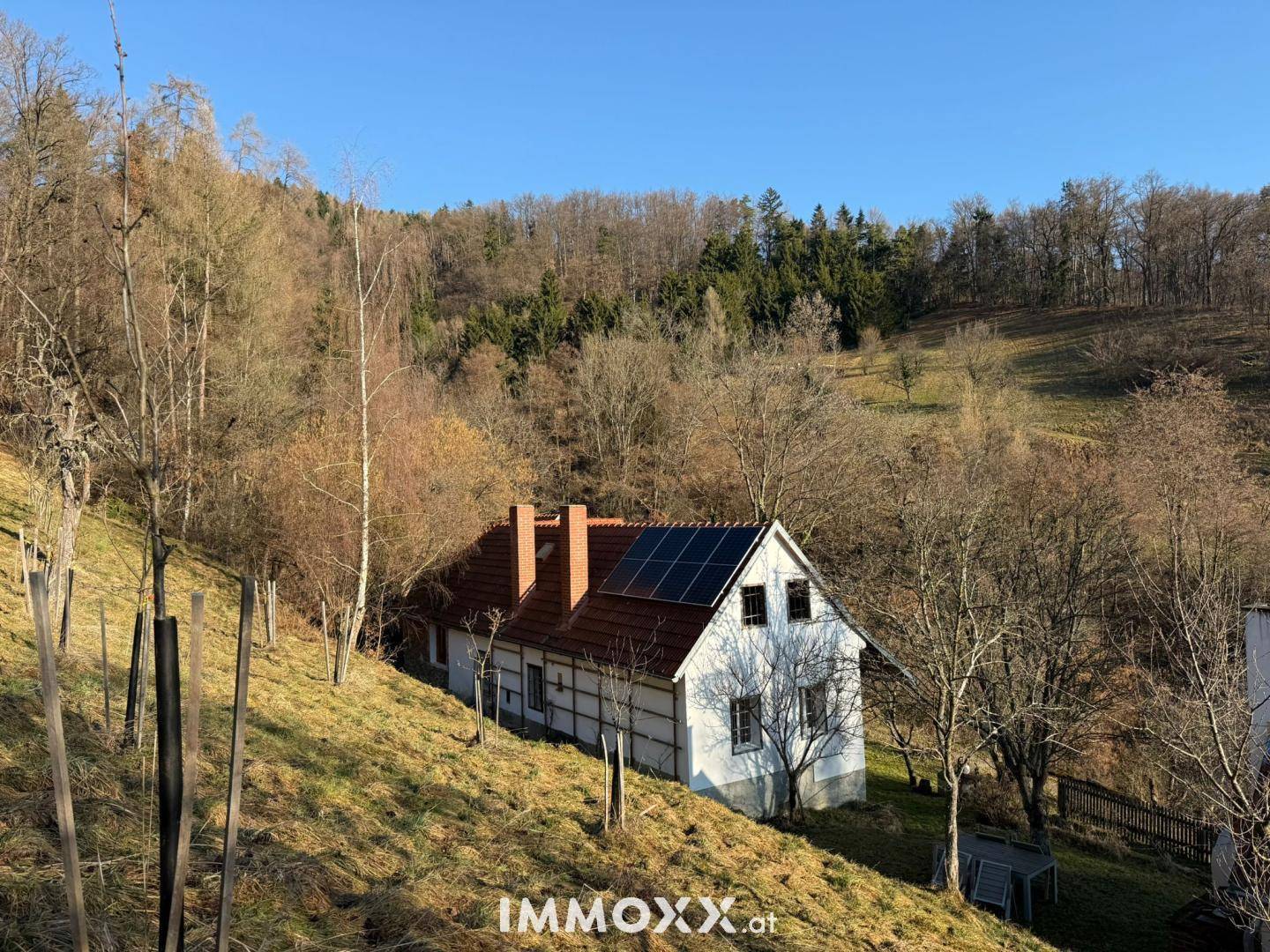 Charmantes Landhaus mit Solarpaneelen auf dem Dach, eingebettet in eine hügelige, bewaldete Landschaft.