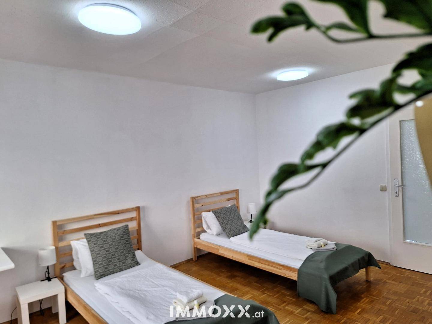 Schlafzimmer mit zwei Einzelbetten, Parkettboden und Deckenleuchten.