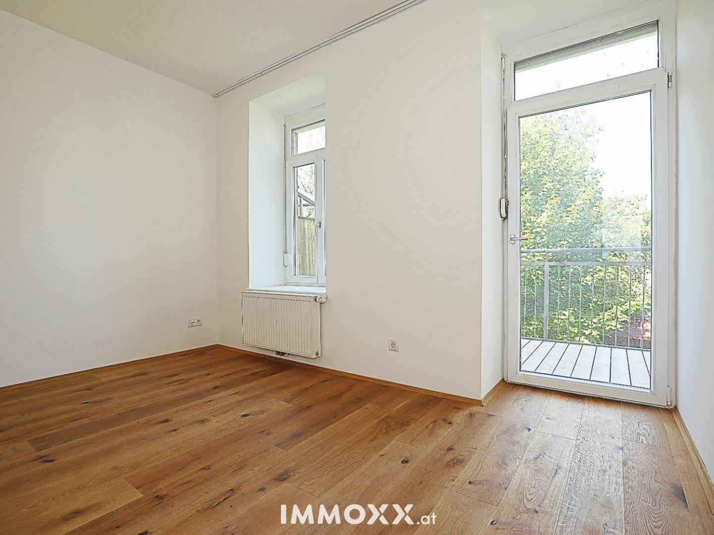 Heller Raum mit Holzboden und großem Fenster mit Balkonzugang, bietet viel Tageslicht.