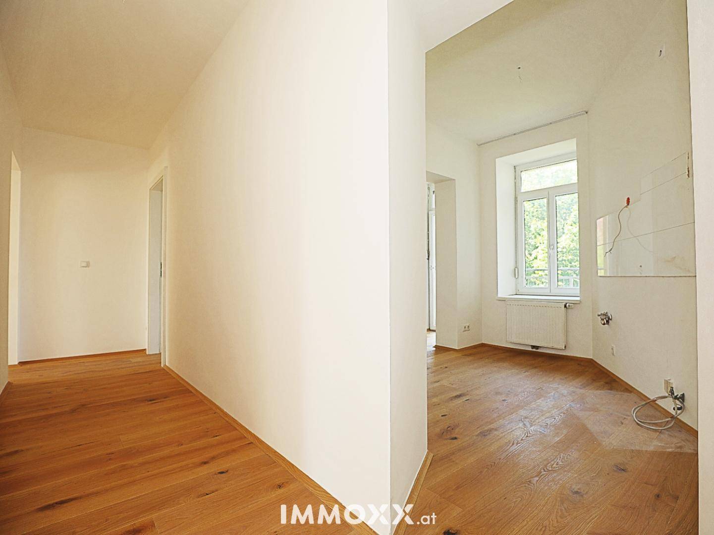 Heller Flur mit Holzboden, der zu einem angrenzenden Raum mit Fenster führt.