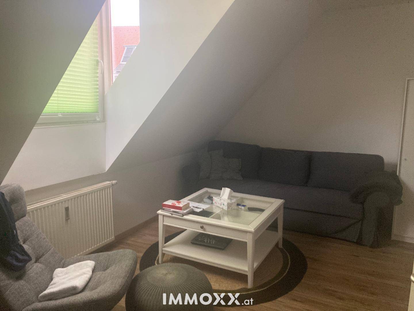 Wohnzimmer im Dachgeschoss mit Sofa, Sessel und Couchtisch, beleuchtet durch ein Fenster.