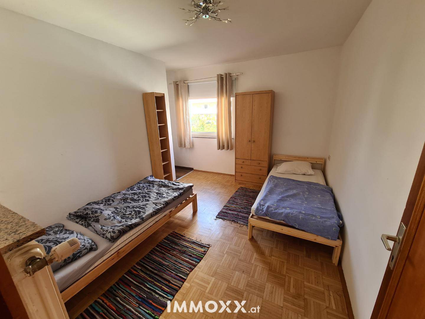 Funktionales Schlafzimmer mit zwei Einzelbetten, Kleiderschrank und klassischem Parkettboden.