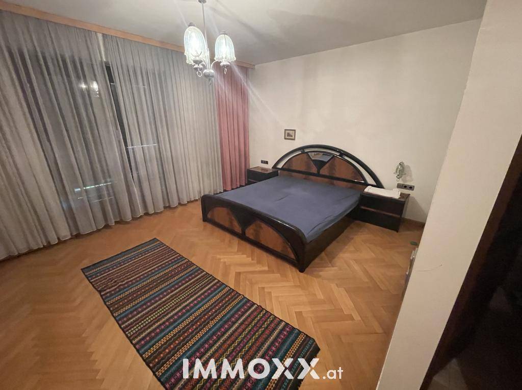 Komfortables Schlafzimmer mit Parkettboden, Doppelbett und großen Fenstern.