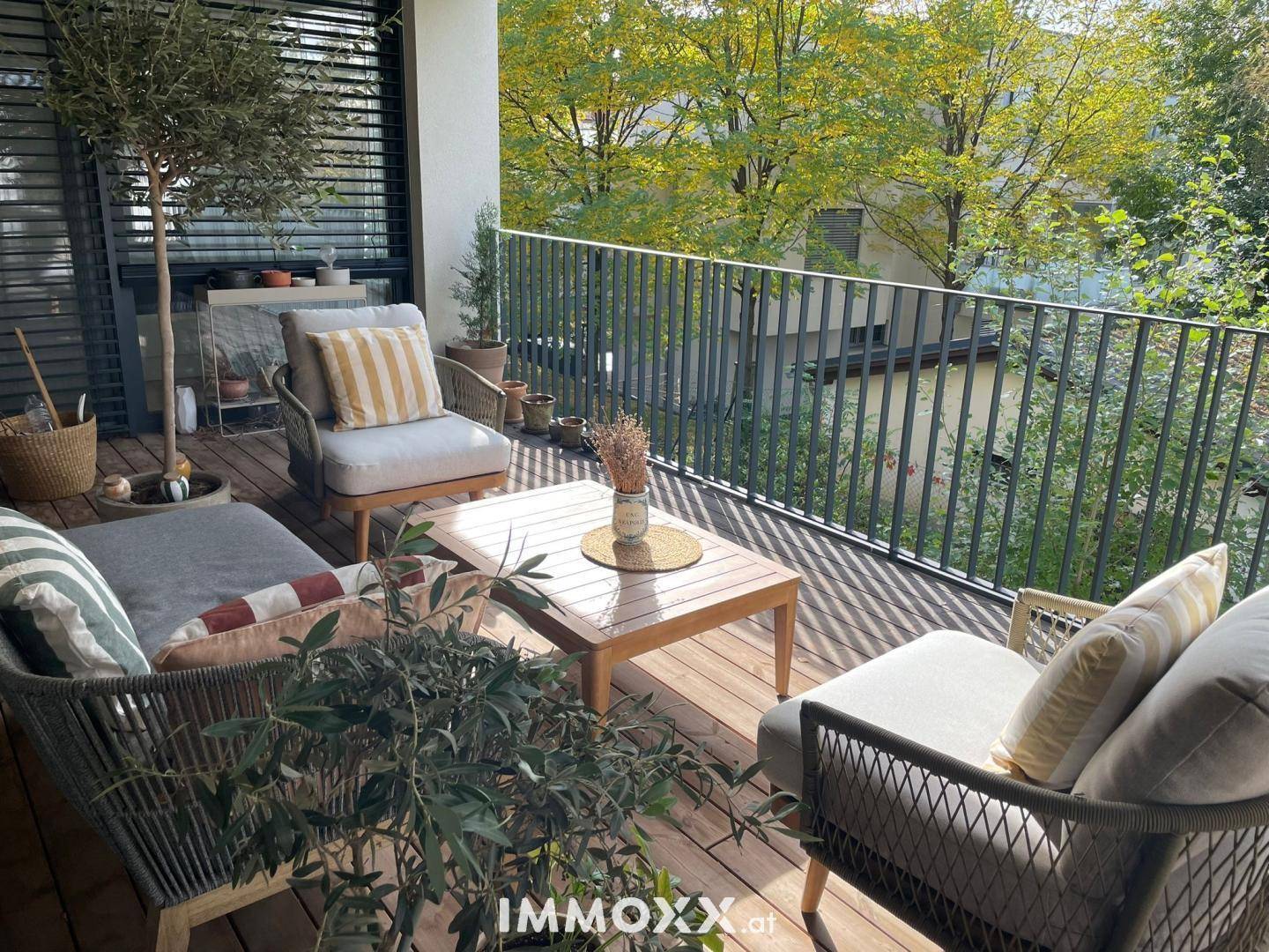 Geräumiger Balkon mit Holzboden, bequemen Sitzgelegenheiten und üppigem Grün im Hintergrund.