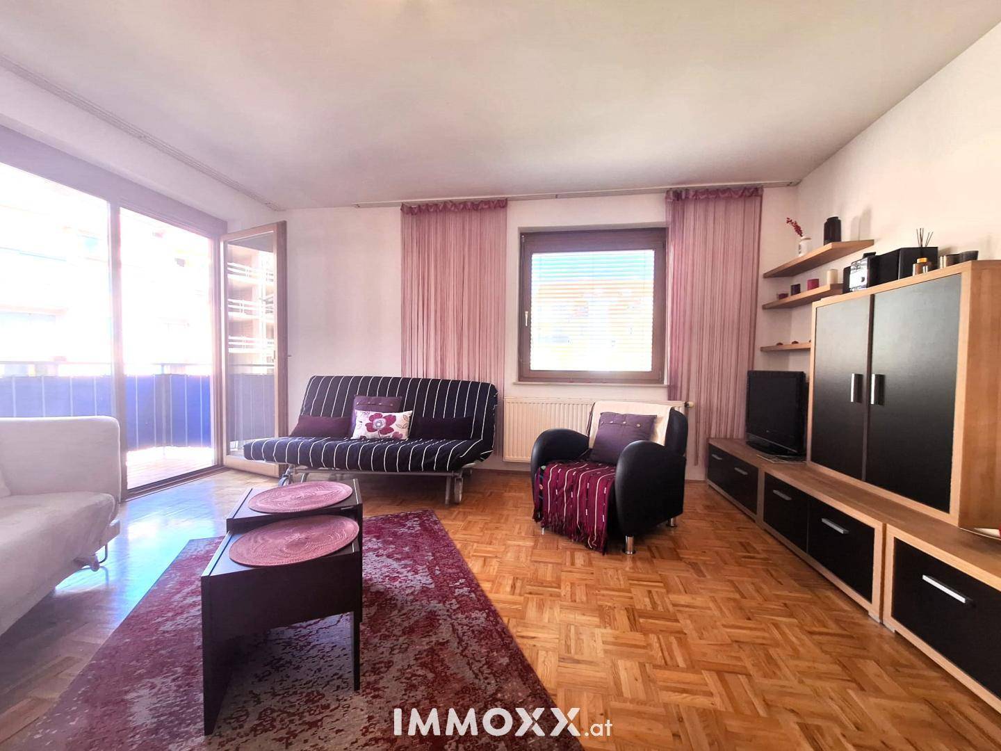 Helles Wohnzimmer mit Parkettboden, Zugang zum Balkon und einer modernen TV-Möbelwand.