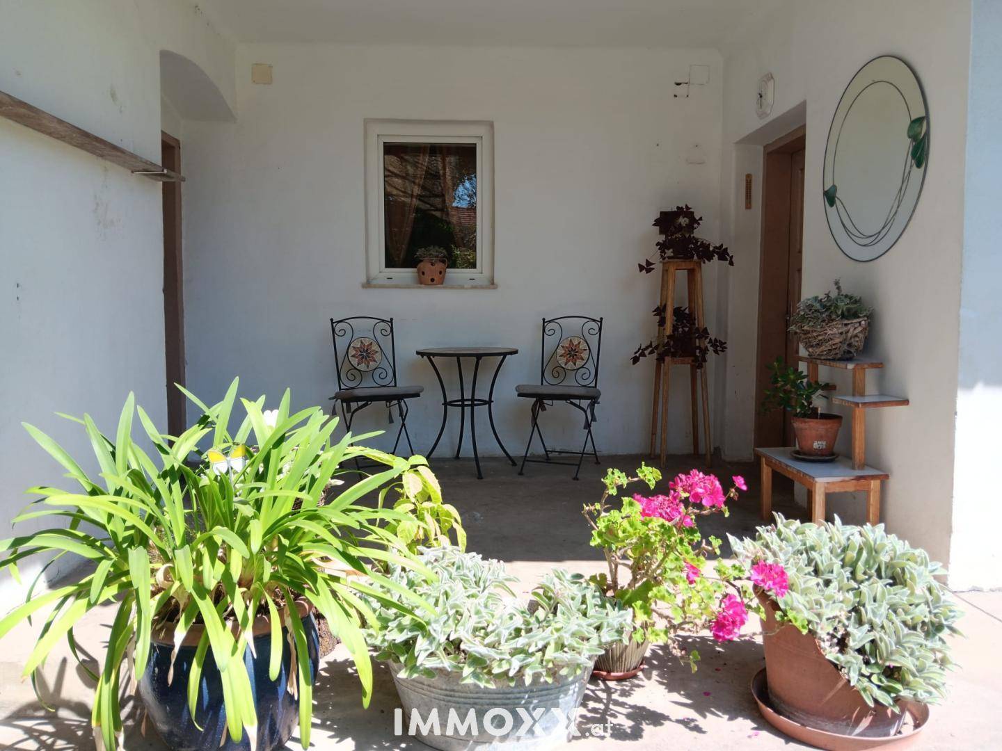 Überdachter Terrassenbereich mit Topfpflanzen und einem kleinen Tisch mit Stühlen.