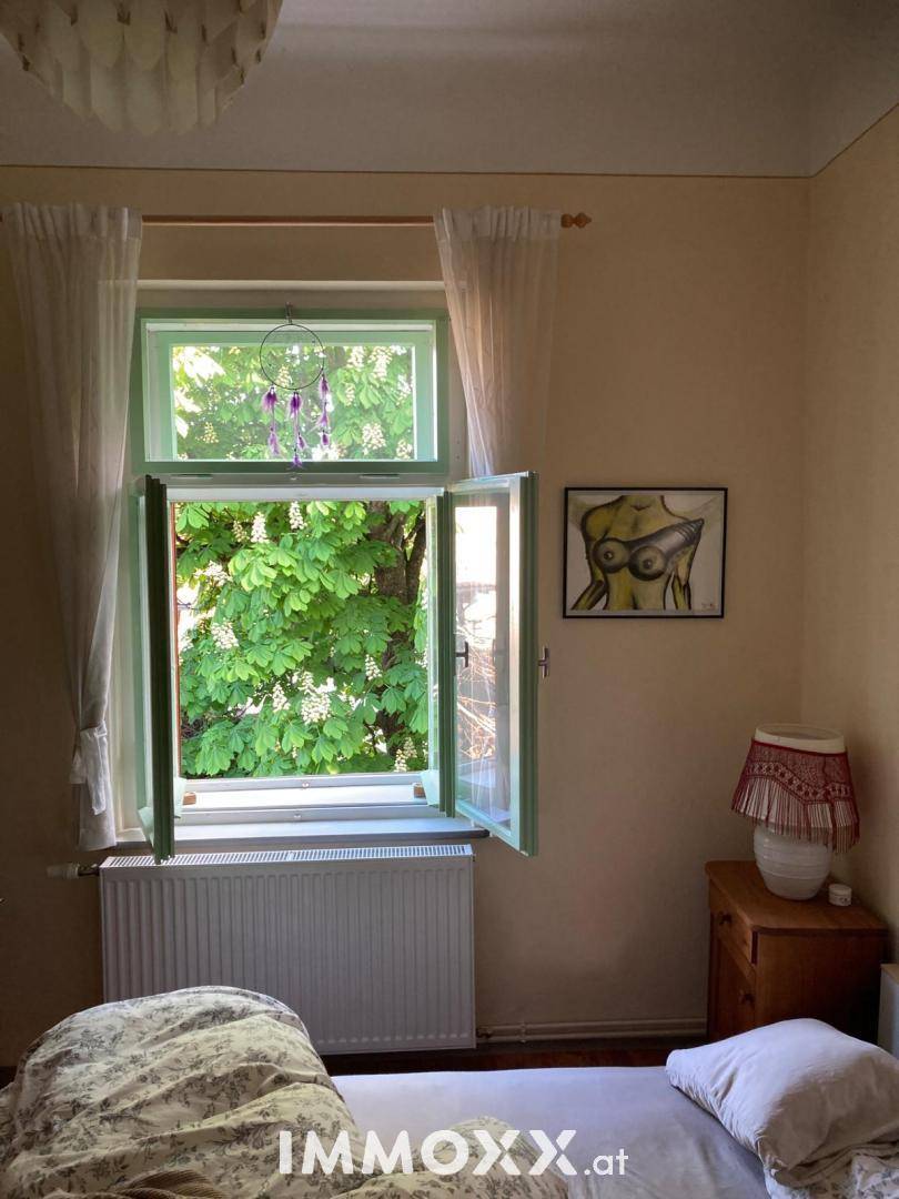 Helles Schlafzimmer mit Blick auf grüne Bäume durch das offene Fenster.
