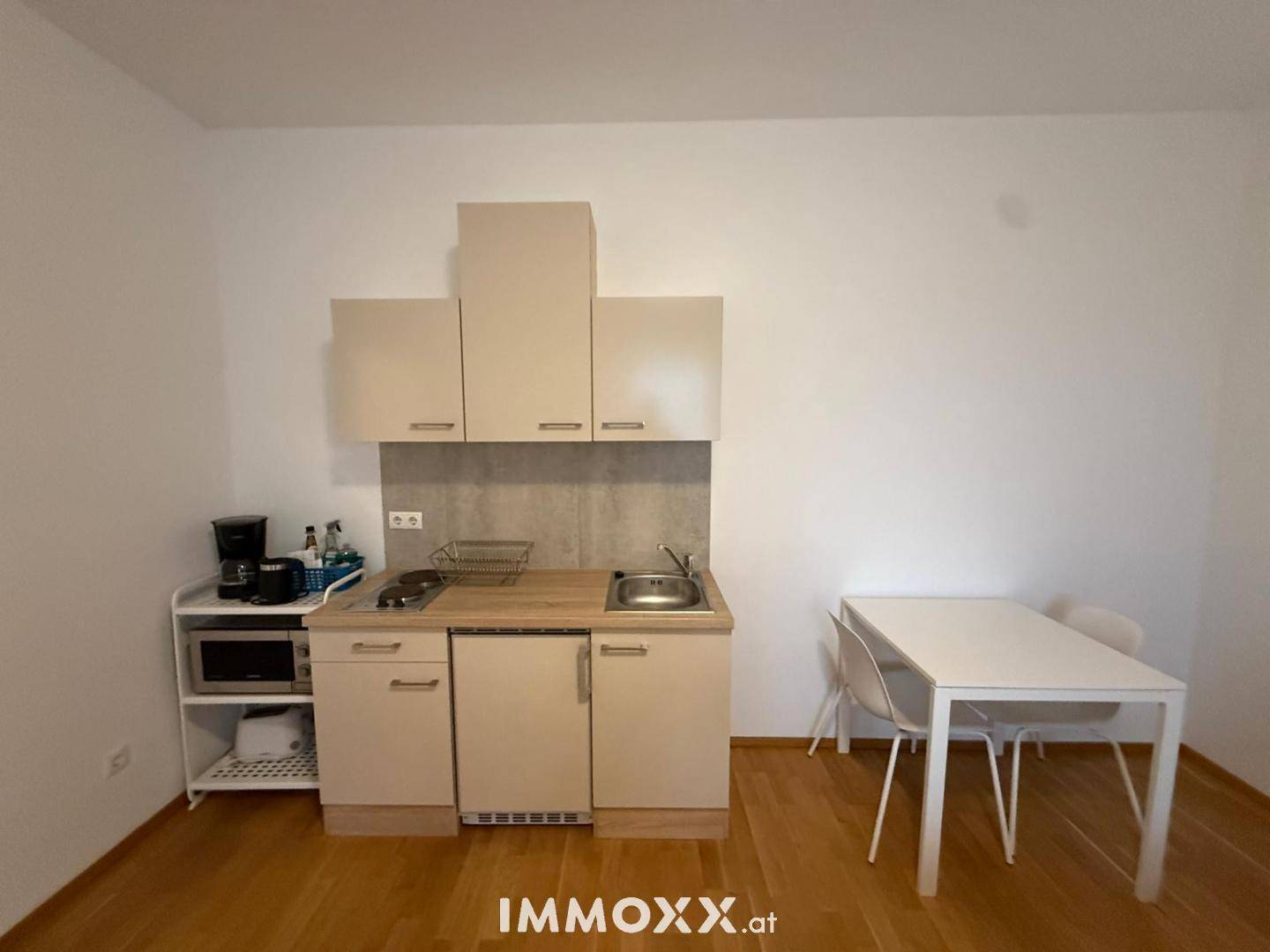Kompakte Küchenzeile mit Esstisch und Stühlen, ideal für kleine Wohnungen mit Holzboden.