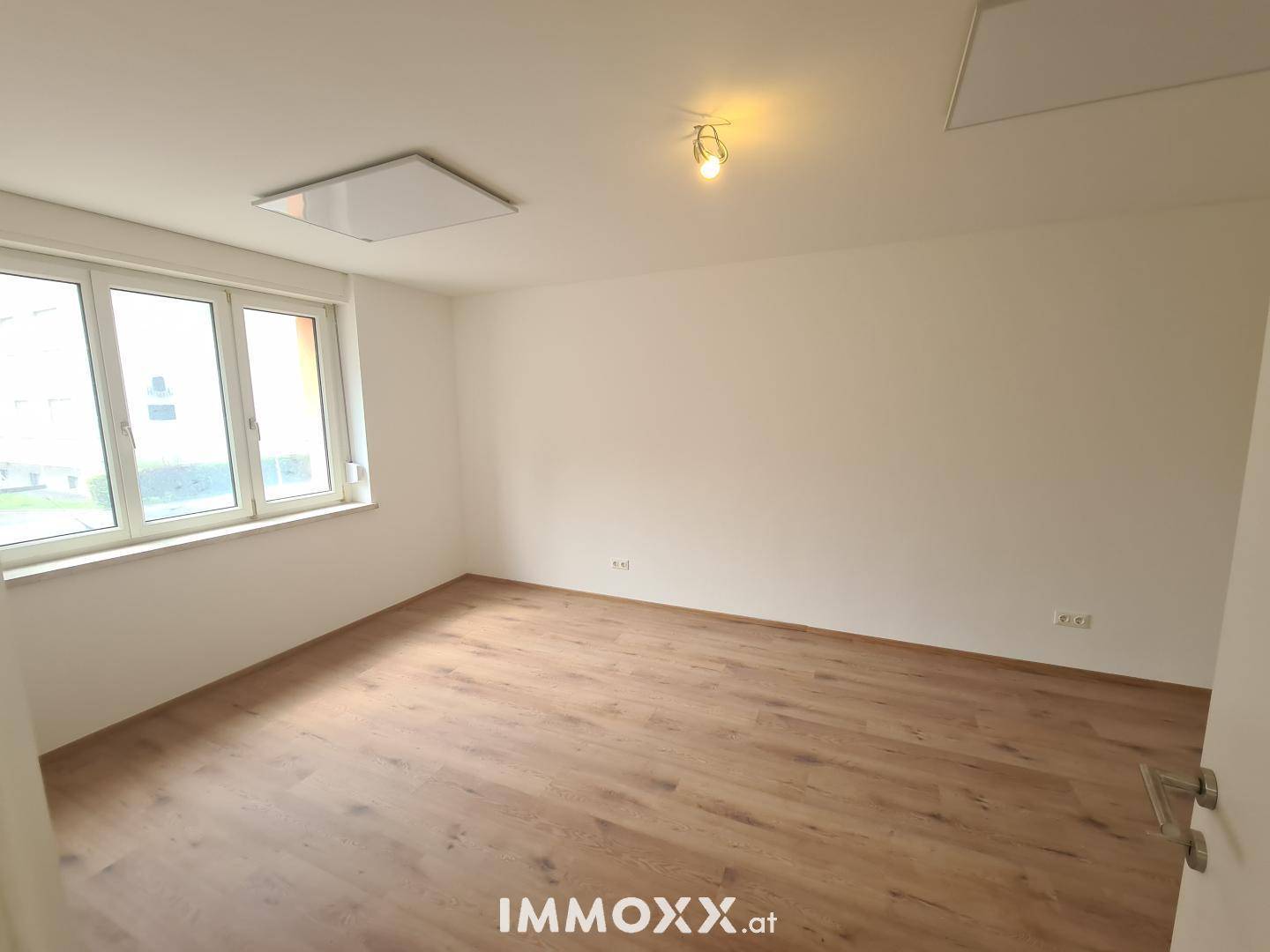 Lichtdurchflutetes Zimmer mit Laminatboden und großen Fenstern, die eine angenehme Atmosphäre schaffen.