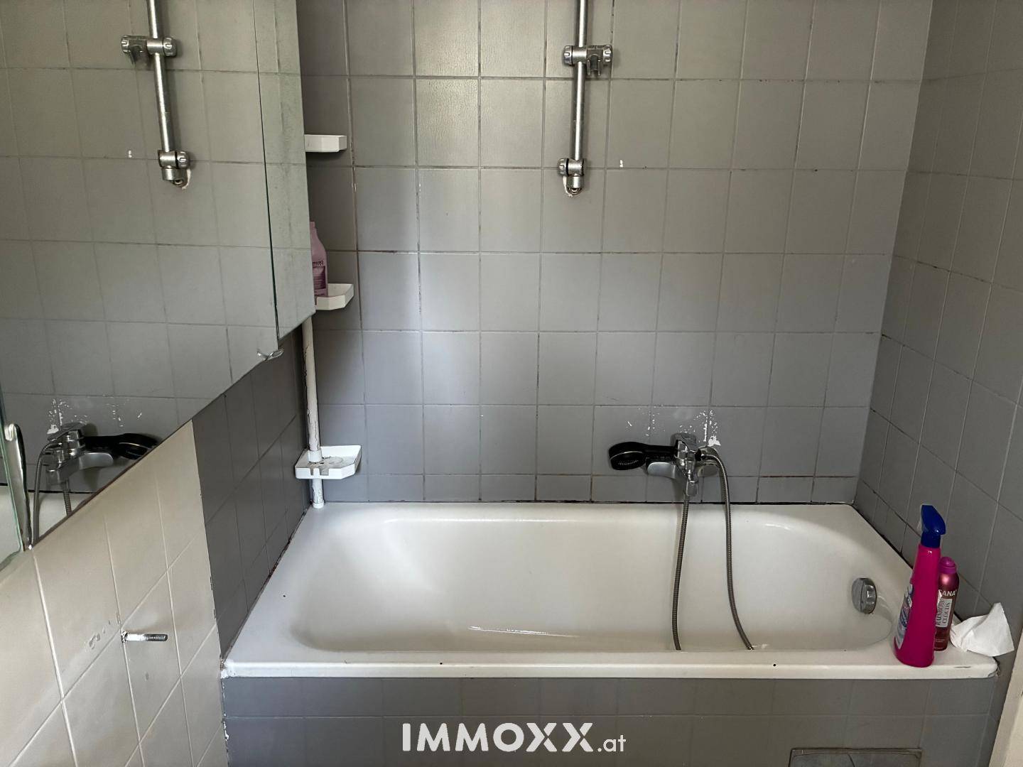 Badezimmer mit Badewanne und grauen Fliesen an den Wänden.