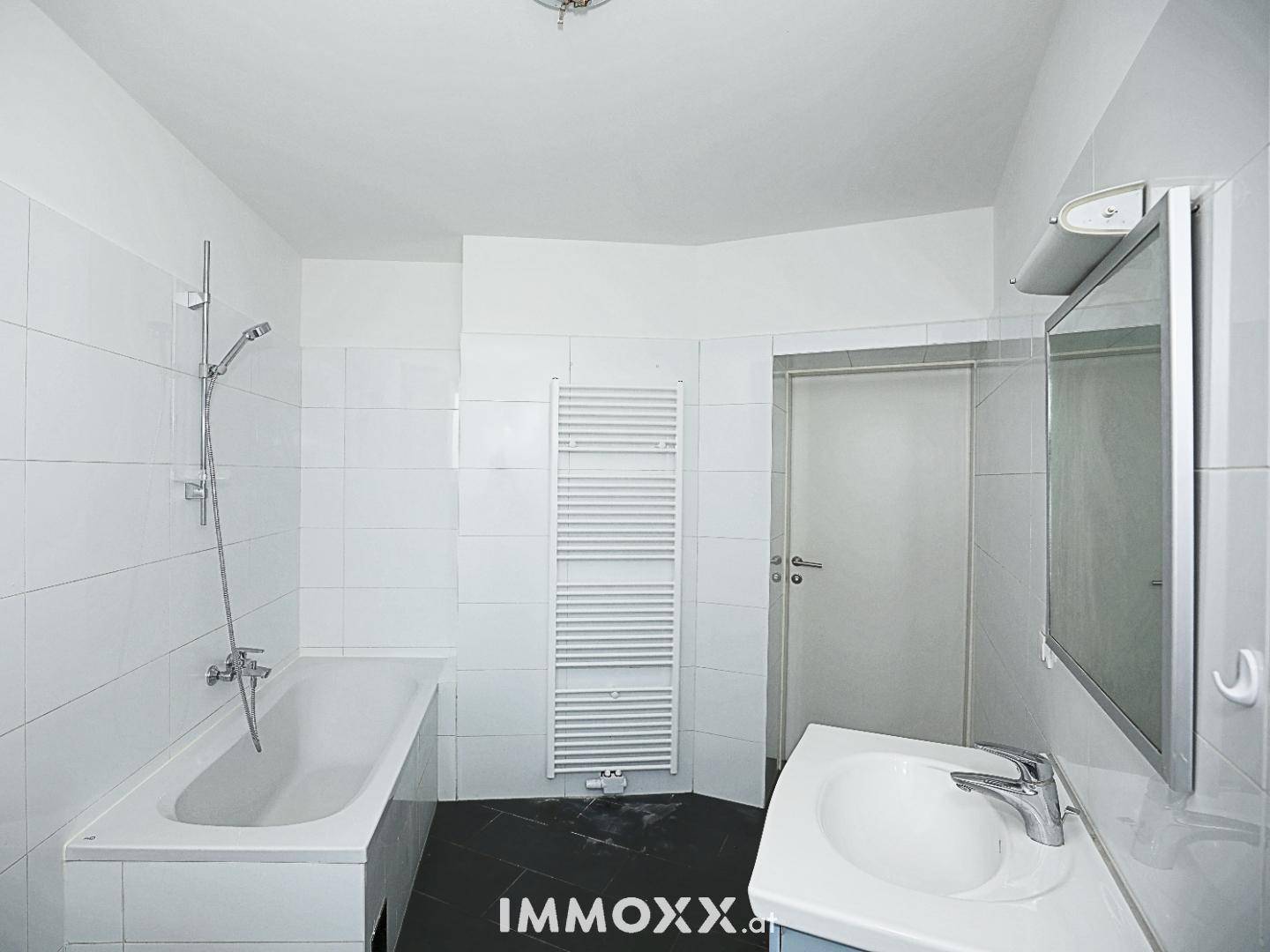 Badezimmer mit Badewanne, Waschbecken, Spiegel und beheiztem Handtuchhalter, alles in Weiß gehalten.