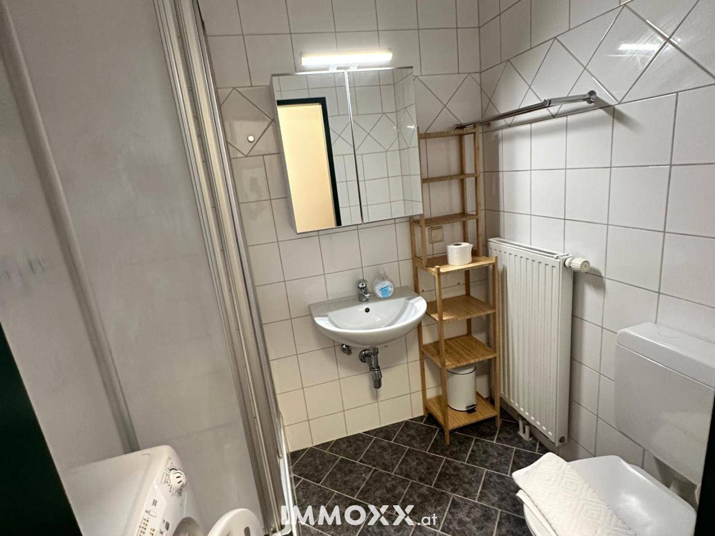 Funktionales Badezimmer mit Duschkabine, Waschbecken, Toilette und Waschmaschine.