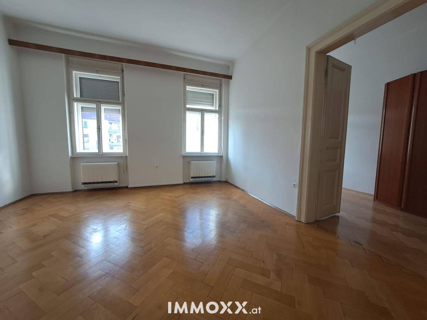 Geräumiges Zimmer mit Fischgrätparkett, zwei Fenstern und einem integrierten Kleiderschrank.
