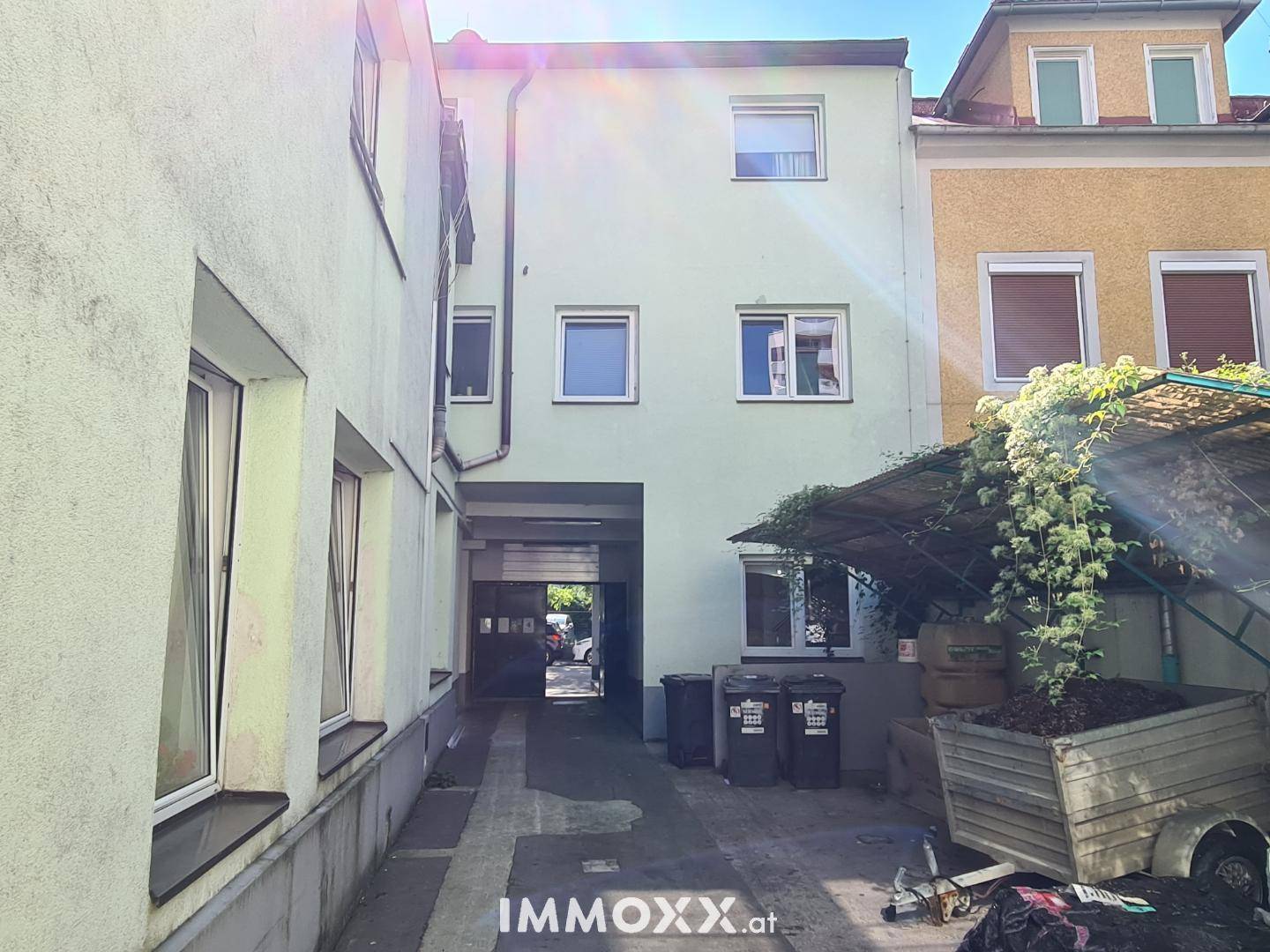 Hinterhofansicht des Gebäudes mit Zufahrt zur Garage und Mülltonnen im Freien.