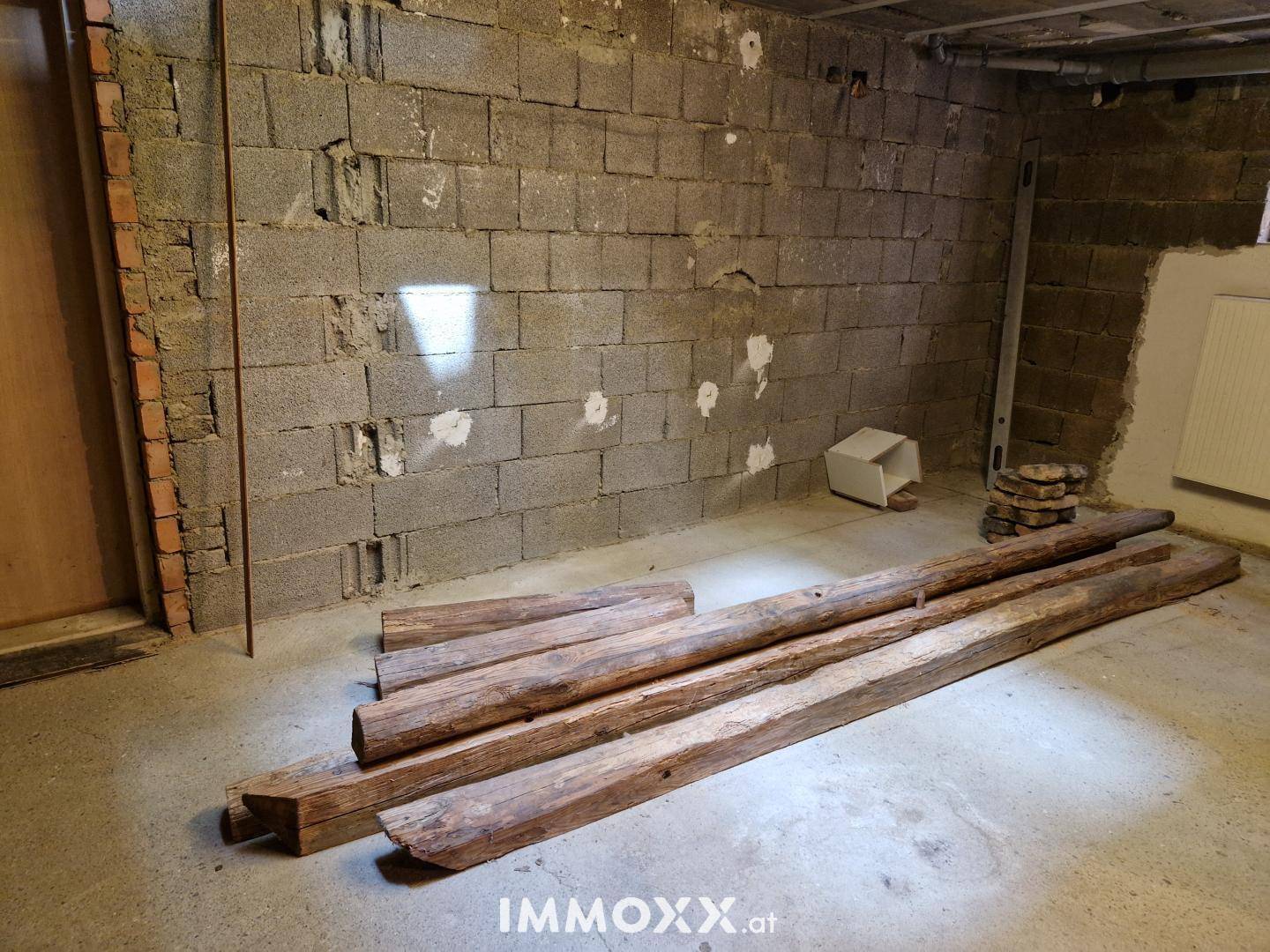 Unfertiger Raum mit Betonsteinwänden und Holzbalken auf dem Betonboden, bereit für den Ausbau.