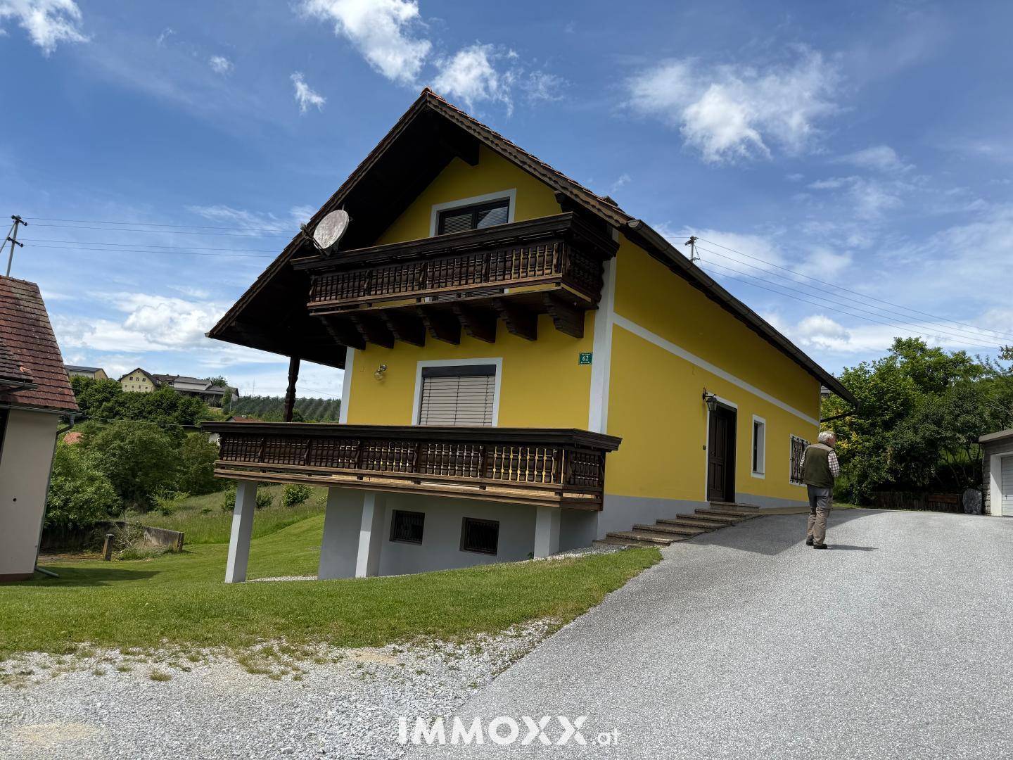 Gelbes Wohnhaus mit traditionellen Holzbalkonen und Zufahrt, eingebettet in eine ländliche Umgebung.