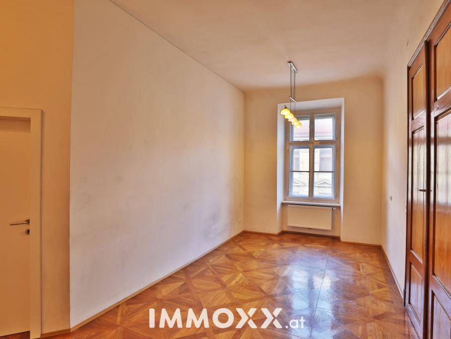 Helles Zimmer mit Parkettboden und einem Fenster, das viel Tageslicht in den Raum bringt.