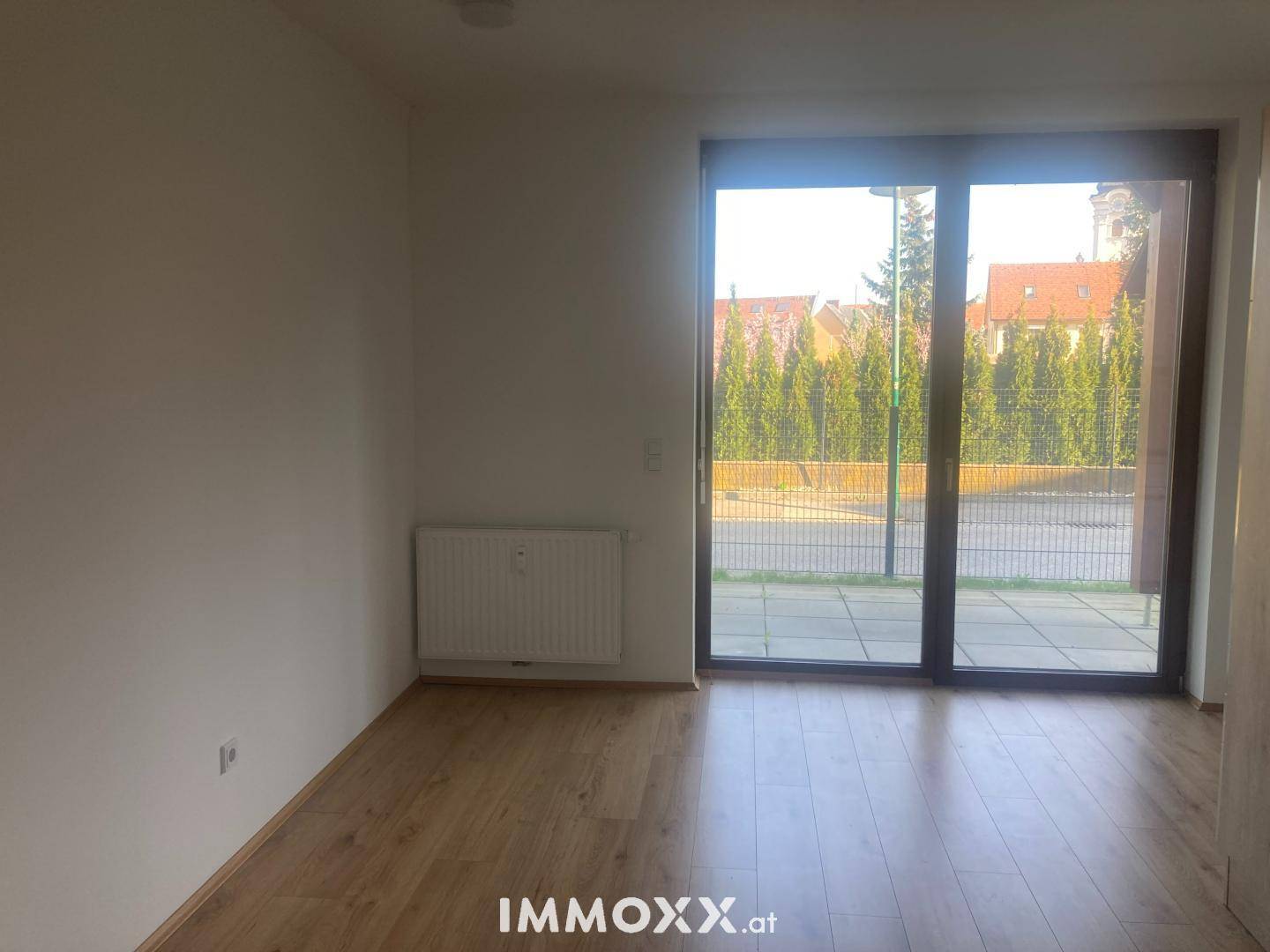 Heller Raum mit Laminatboden und großer Terrassentür, die viel Tageslicht hereinlässt.