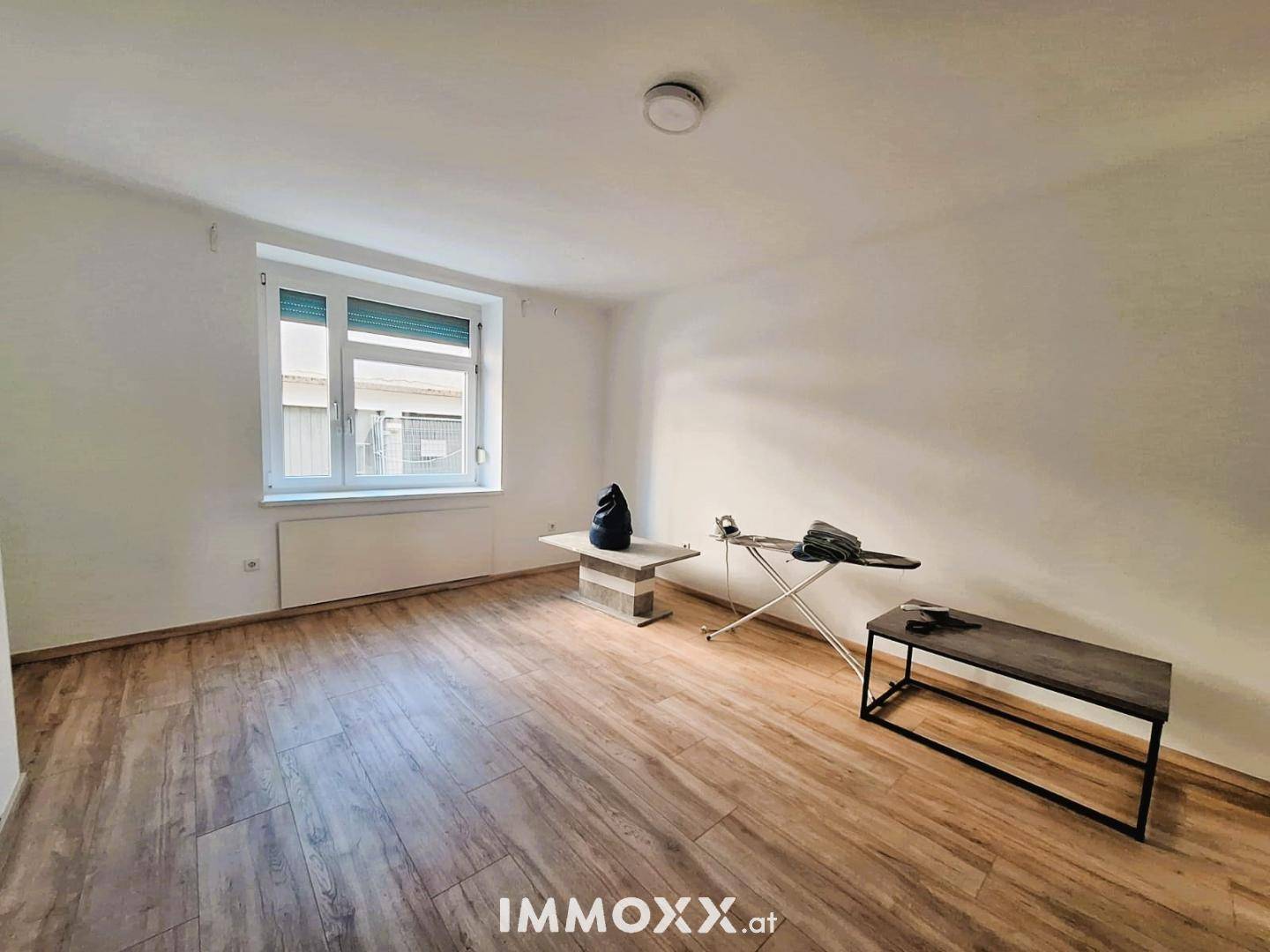 Geräumiger, heller Raum mit Laminatboden und einem Fenster, das viel Tageslicht hereinlässt.