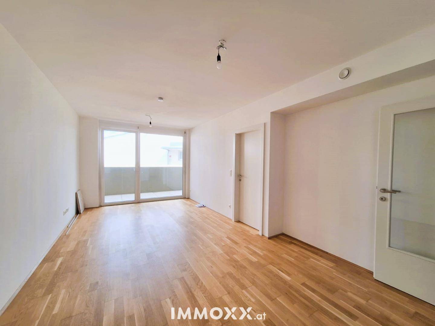 Geräumiges Wohnzimmer mit Holzboden und Zugang zu einem Balkon, bereit zur Einrichtung.