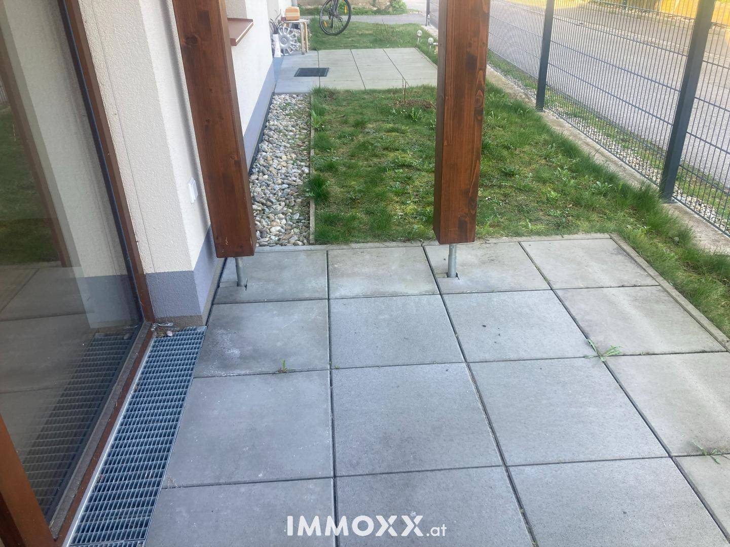 Kleine gepflasterte Terrasse mit Zugang zum Gartenbereich, umgeben von einem Zaun.