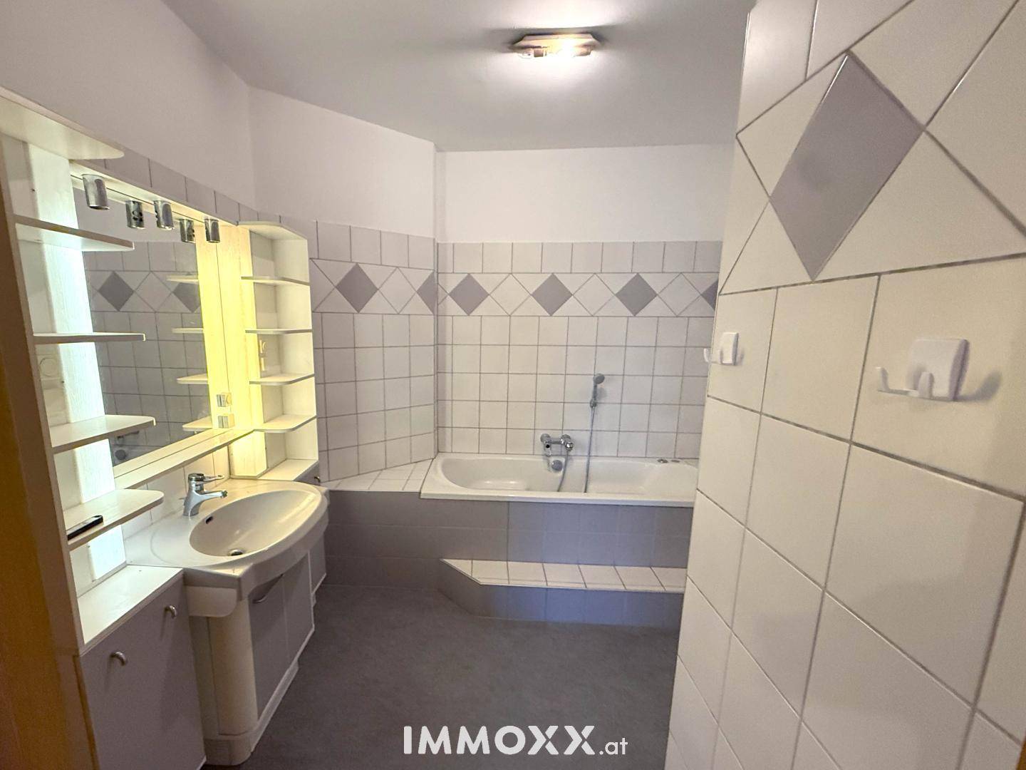Badezimmer mit weiß-grauen Fliesen, eingebauter Badewanne und Waschtisch mit großem Spiegel.