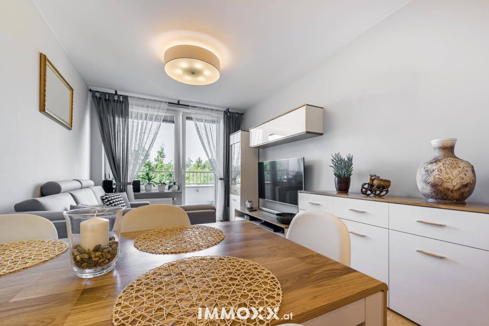 Heller Wohn- und Essbereich mit Holztisch, Sofa und Zugang zum Balkon.