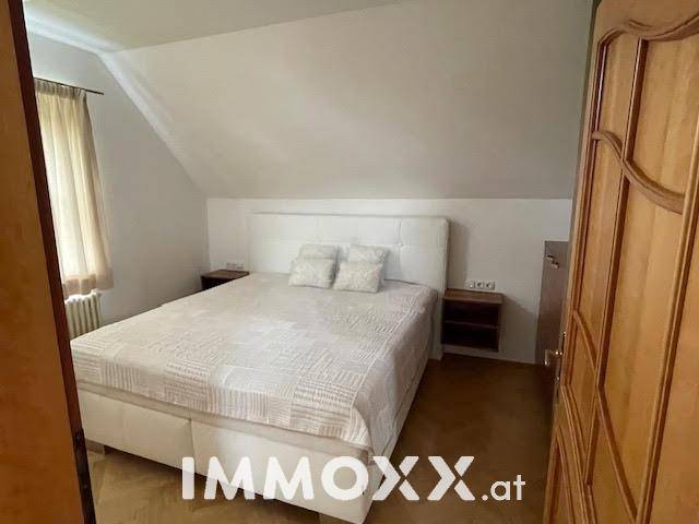 Helles Schlafzimmer im Dachgeschoss mit Doppelbett, Parkettboden und schrägen Wänden.
