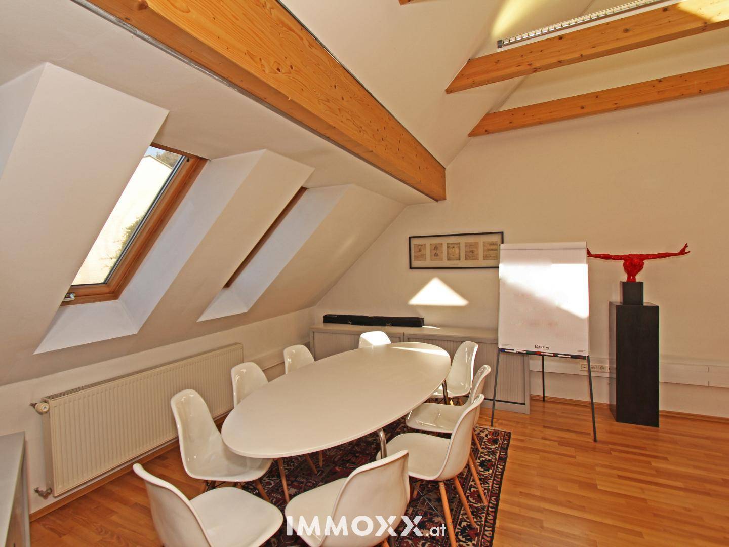 Konferenzbereich im Dachgeschossbüro mit ovalem Tisch, weißen Stühlen und Dachfenstern.