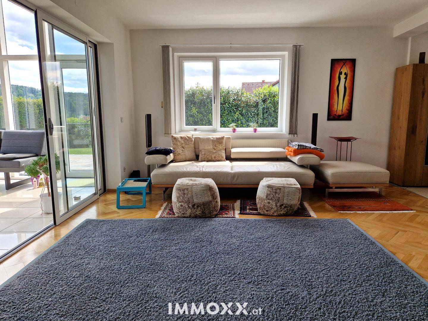 Helles Wohnzimmer mit beigem Sofa, großem Teppich und Blick auf den angrenzenden Wintergarten.