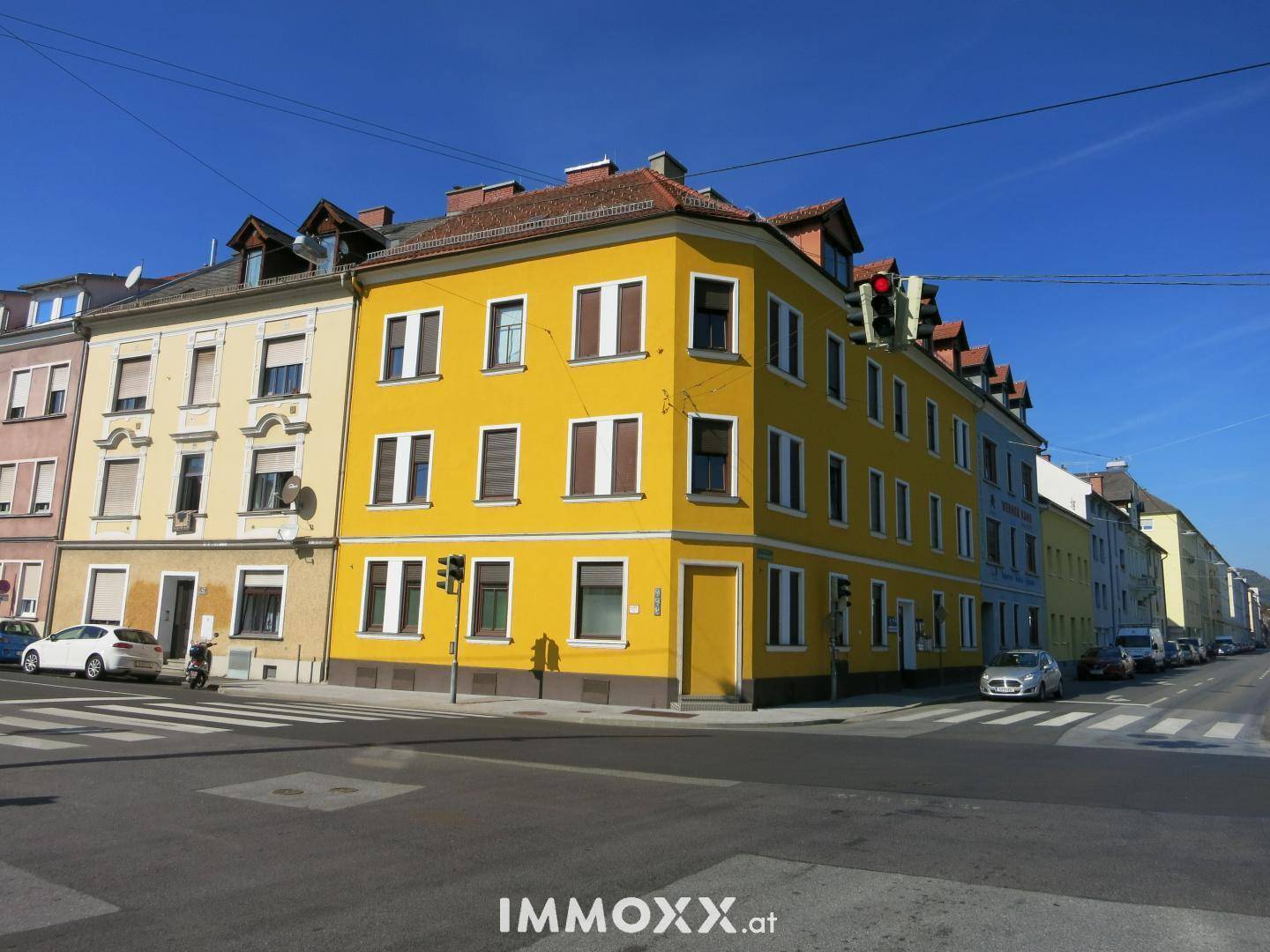 Gelbes Eckgebäude mit vielen Fenstern an einer städtischen Kreuzung unter blauem Himmel.