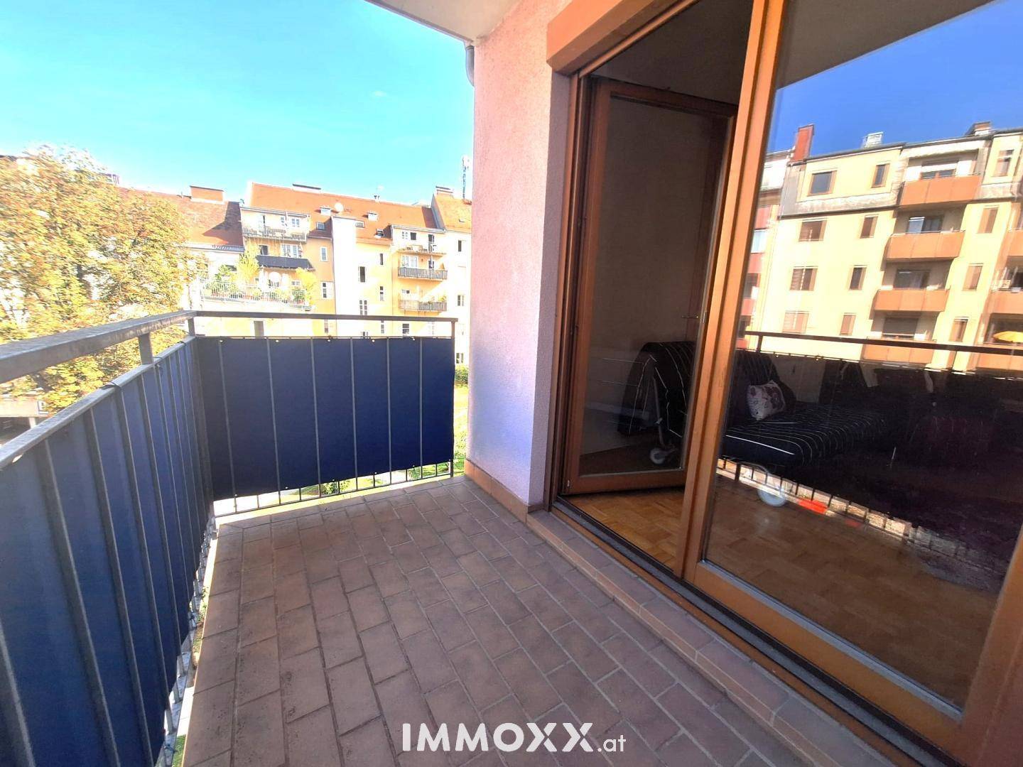 Sonniger Balkon mit Fliesenboden und Blick auf die umliegenden Gebäude und Bäume.