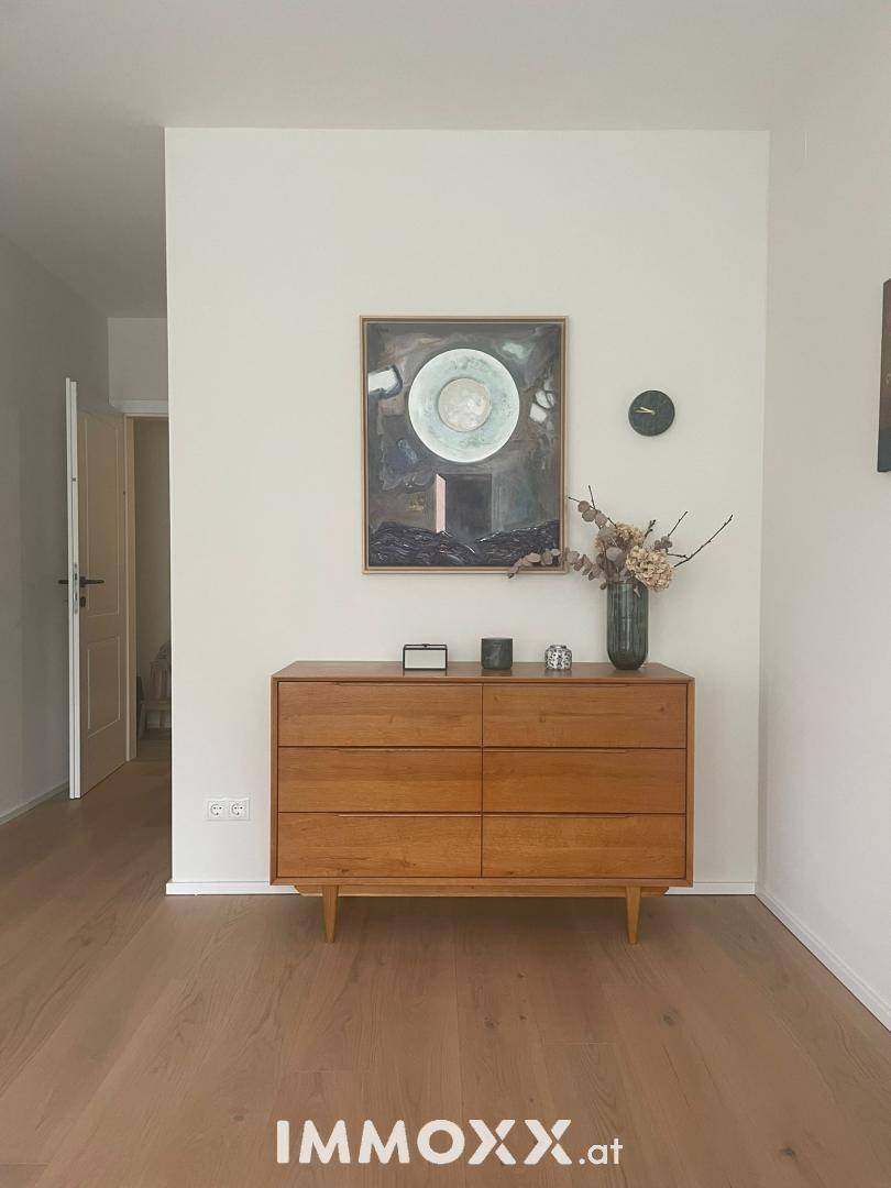 Heller Flur mit Holzboden und einer eleganten Kommode, geschmackvoll dekoriert.
