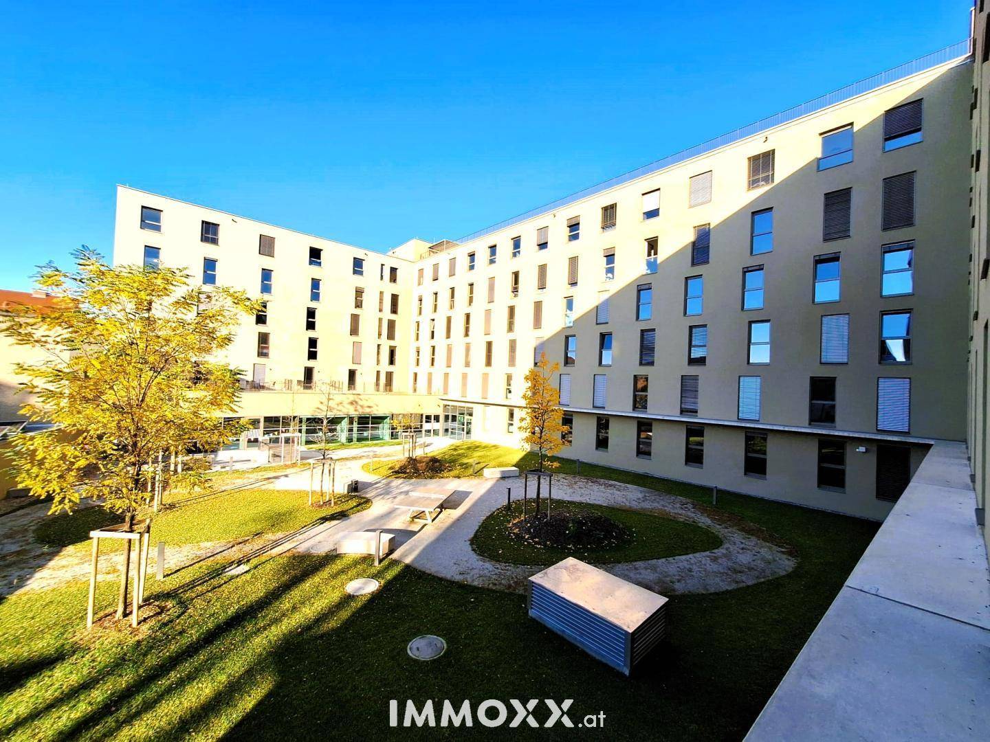 Moderner Gebäudekomplex mit gepflegtem Innenhof und Grünflächen unter blauem Himmel.