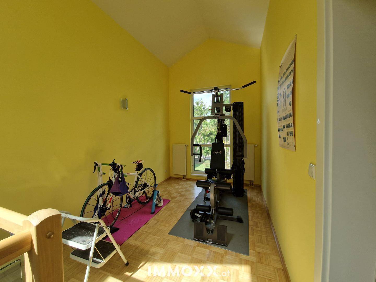 Fitnessraum mit gelben Wänden, Parkettboden und verschiedenen Trainingsgeräten unter einer Dachschräge.