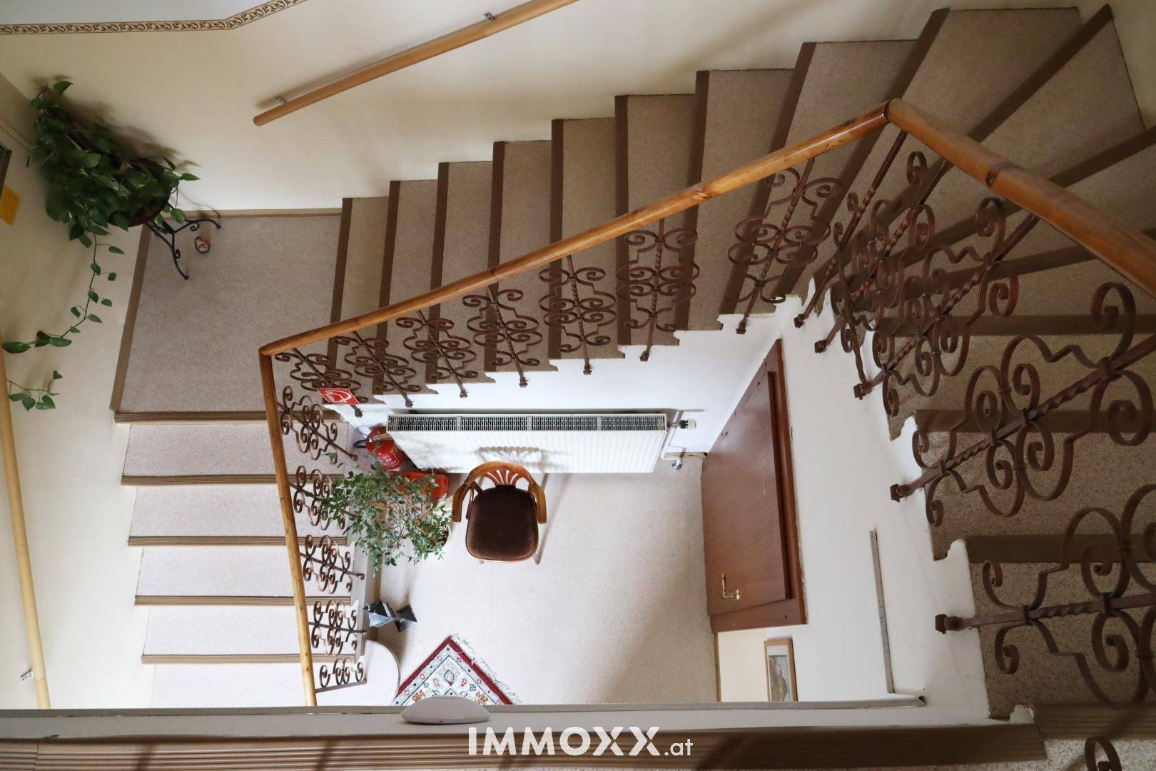 Blick von oben auf eine geschwungene Treppe mit Teppich und schmiedeeisernem Geländer.