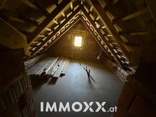 Hoher Dachboden mit freiliegenden Holzbalken und einem kleinen Fenster, das natürliches Licht hereinlässt.