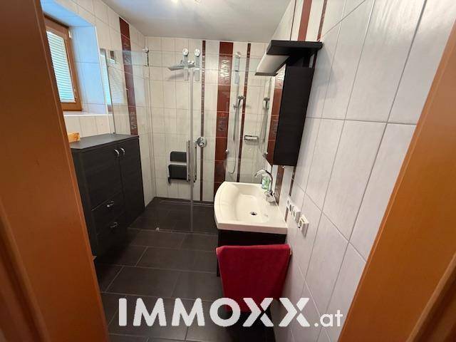 Modernisiertes Badezimmer mit Dusche, Waschbecken und rot-weißen Fliesen, ausgestattet mit einem Fenster.