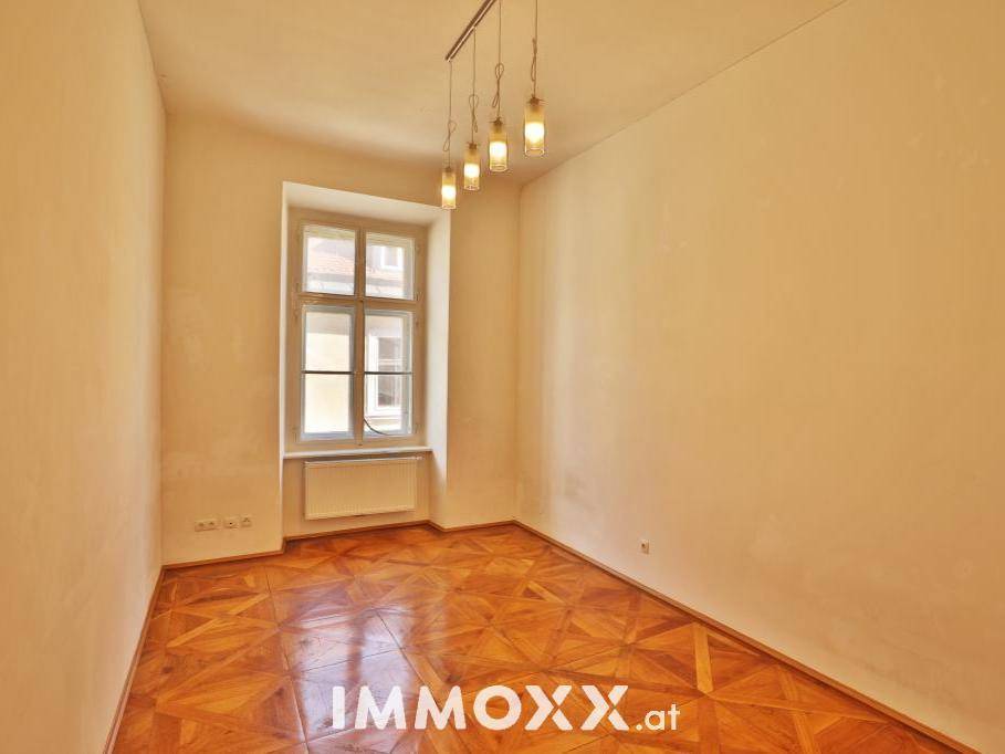 Helles Zimmer mit Fischgrätparkettboden und einem Fenster, das viel Tageslicht hereinlässt.
