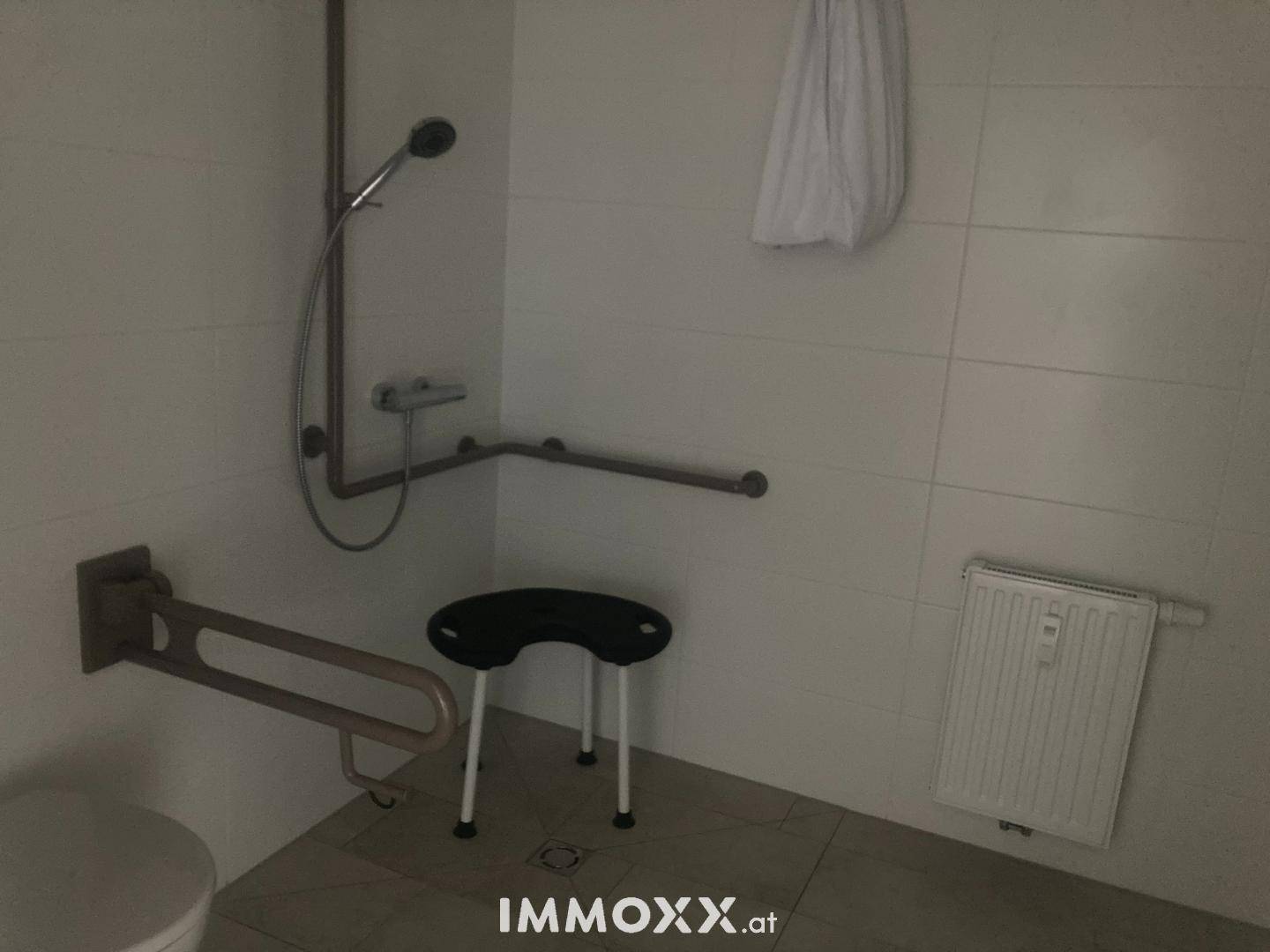 Barrierefreies Badezimmer mit Duschbereich, Haltegriffen und einem Heizkörper.