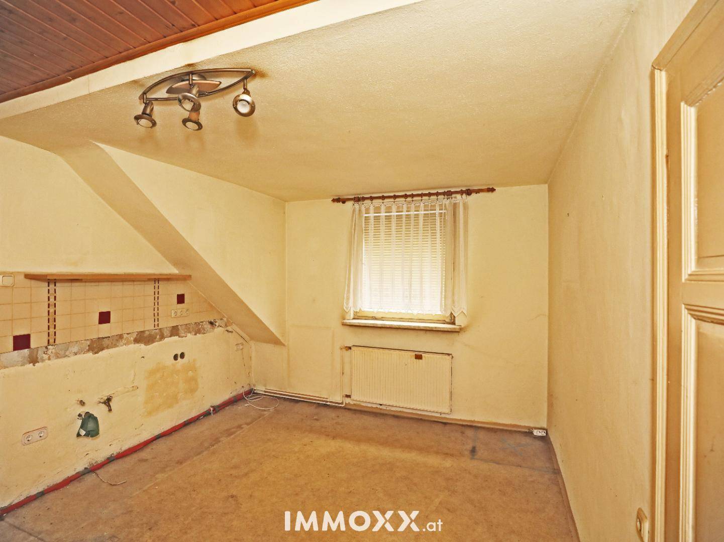 Raum mit Holzdecke und Fliesenresten an der Wand, vorbereitet für eine neue Küche.
