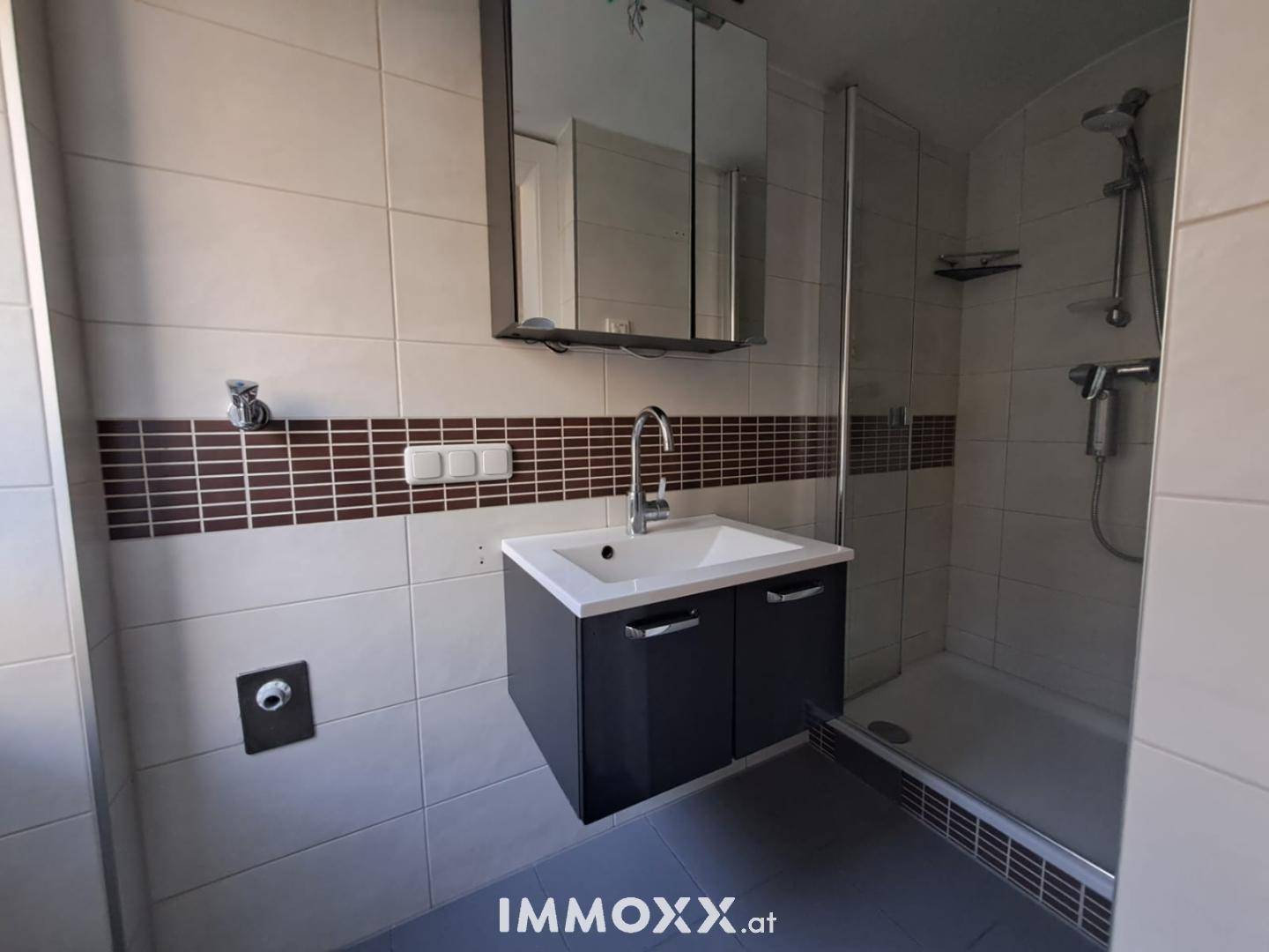 Modernes Badezimmer mit Duschkabine, Einzelwaschbecken und Wandfliesen in zwei Farbtönen.