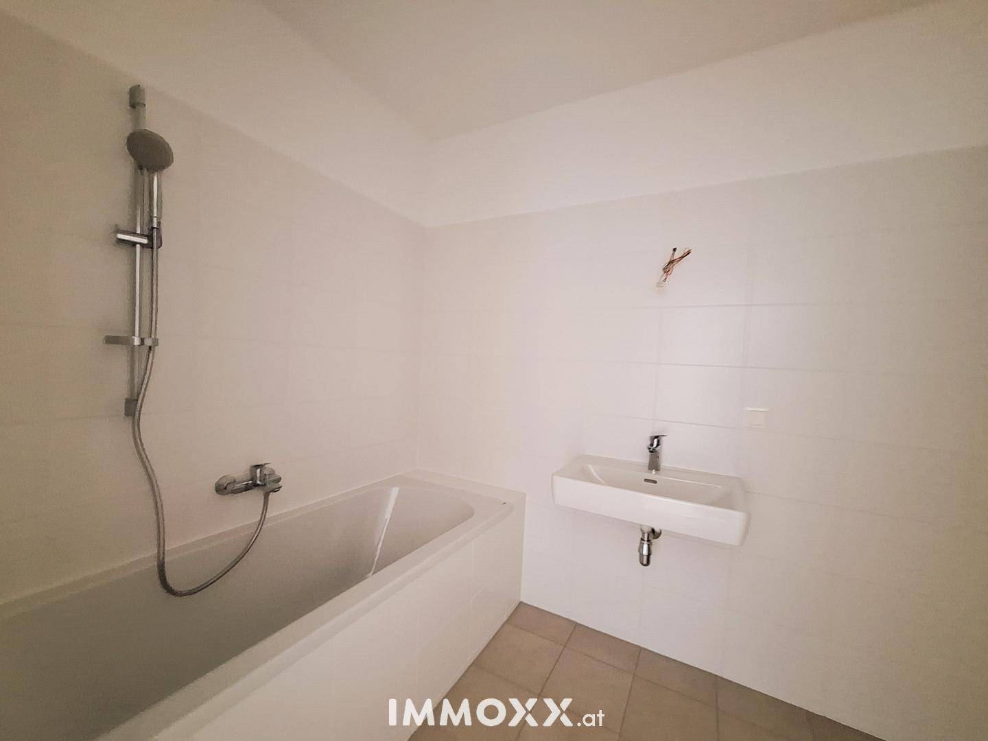 Modernes Badezimmer mit Badewanne, Duscharmatur und Wandwaschbecken, weiß gefliest.
