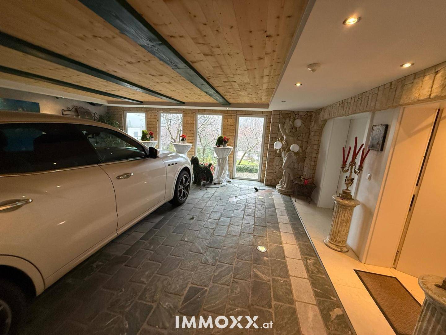Geräumige Garage mit Steinboden, Holzdecke und großen Fenstern, die auch als Mehrzweckraum dient.