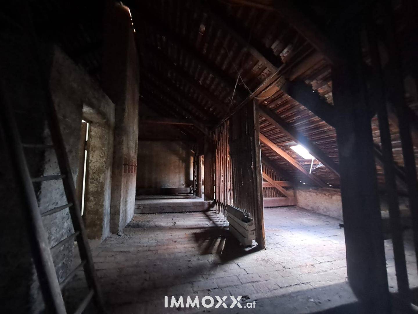 Geräumiger, unausgebauter Dachboden mit Holzbalken und einem Dachfenster für natürliches Licht.